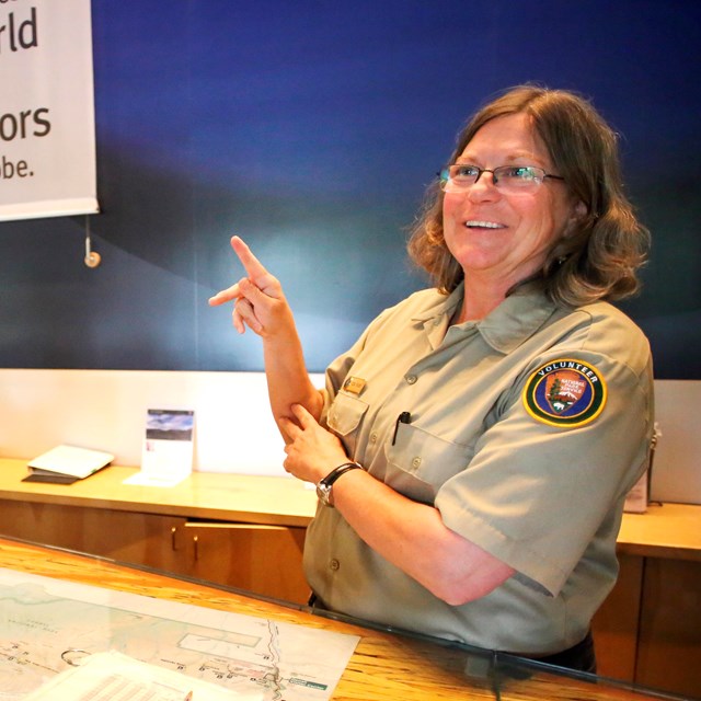 A person in an NPS volunteer uniform makes the letter K in American Sign Language with their hands.