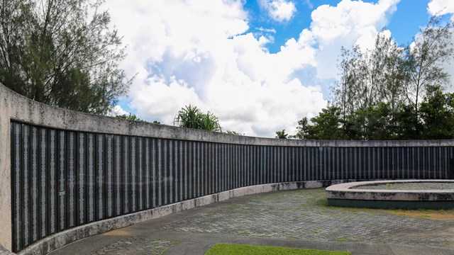 A long curved concrete wall with inset black plaques covered in engraved names.