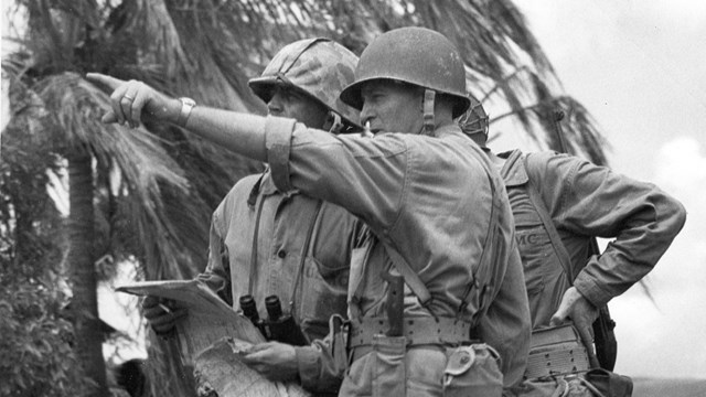 Three soldiers stand together, consulting a map. One soldier is pointing.