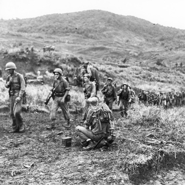 Line of soldiers marching single file along a path up a hill.