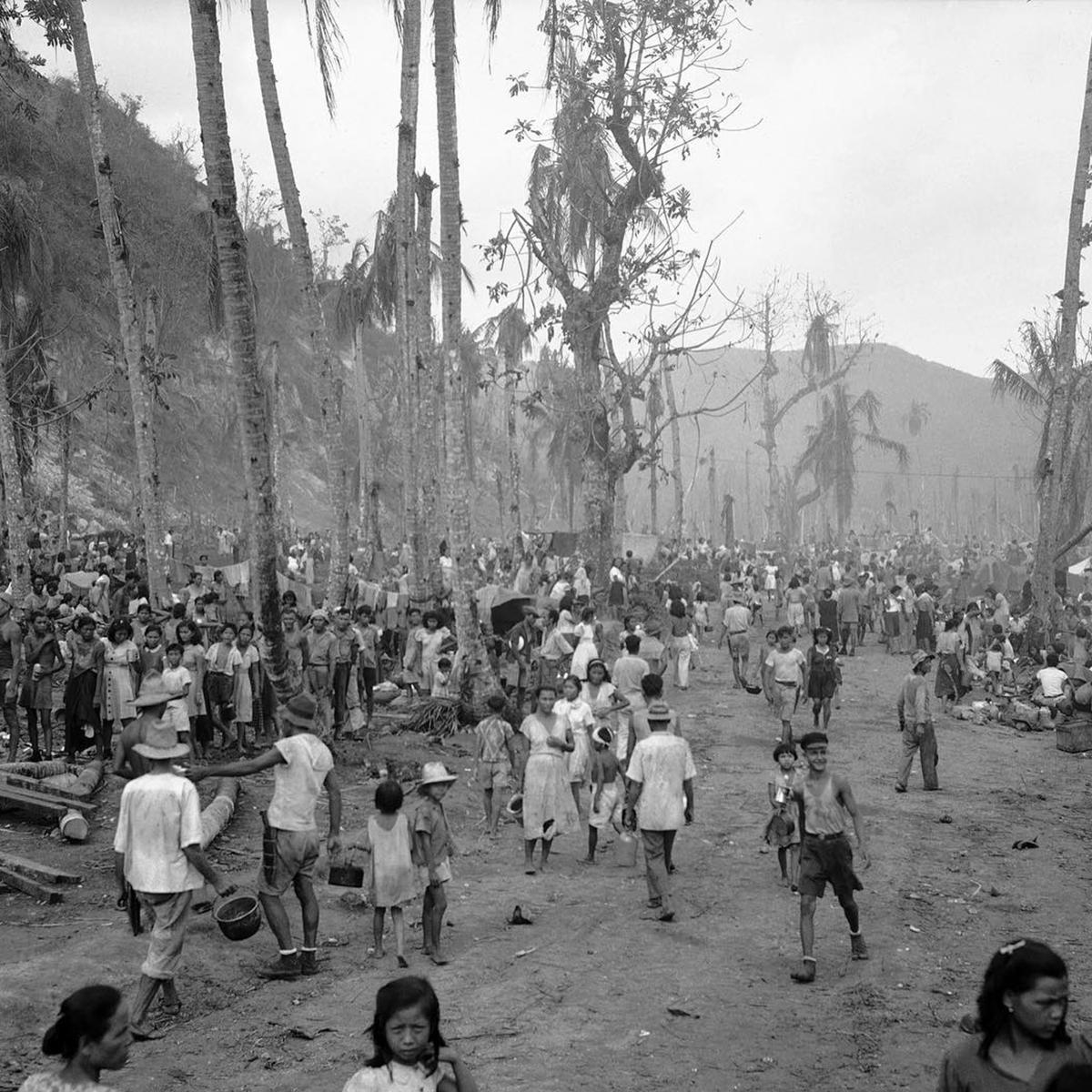 Hundreds of people wearing ragged clothes in a clearing in the jungle