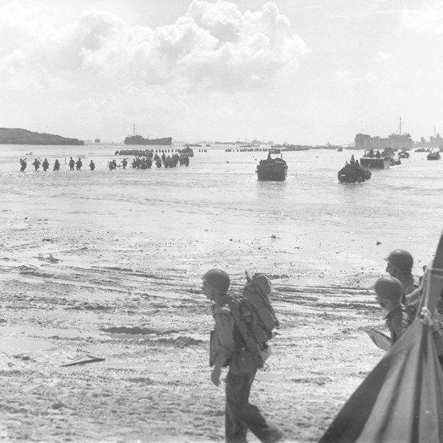 Soldiers wade through shallow waters toward the beach.