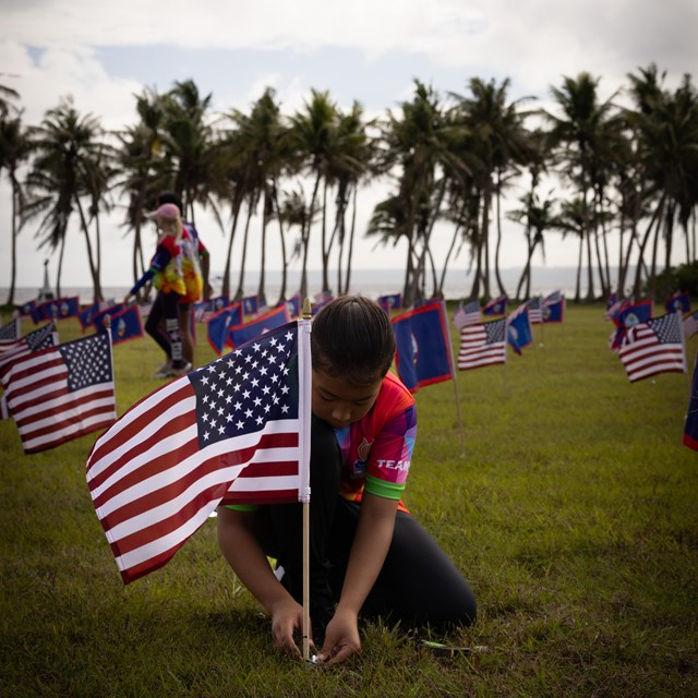 Young Pacific Islander girl placing US flags in a large field