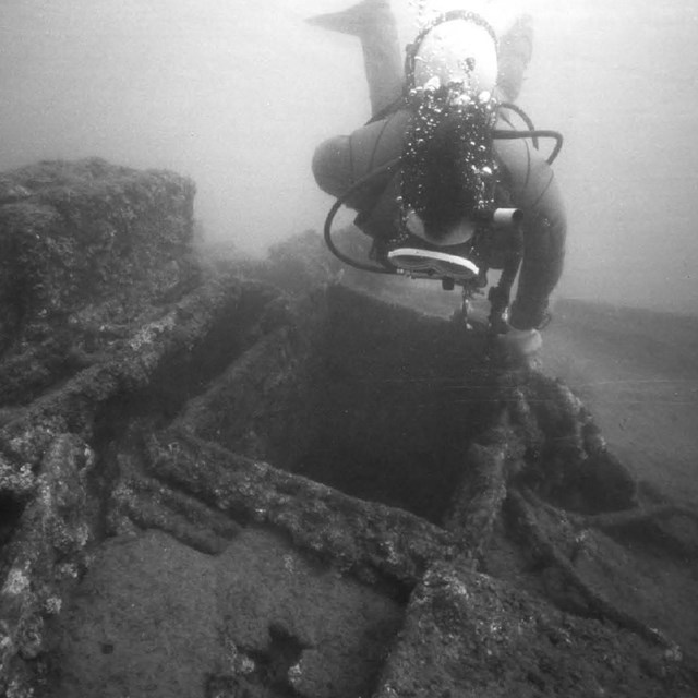 Black and white photo of a scuba diver examining a sunken ship