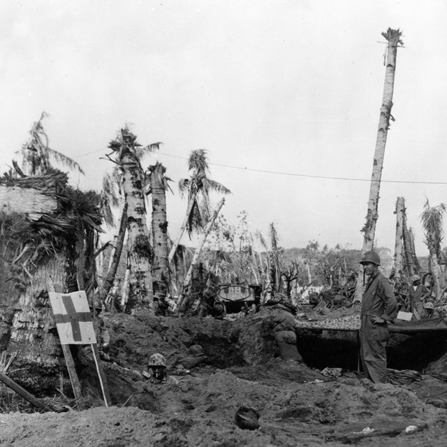 A sign with a cross on it next to a group of soldiers on a bombed out beach