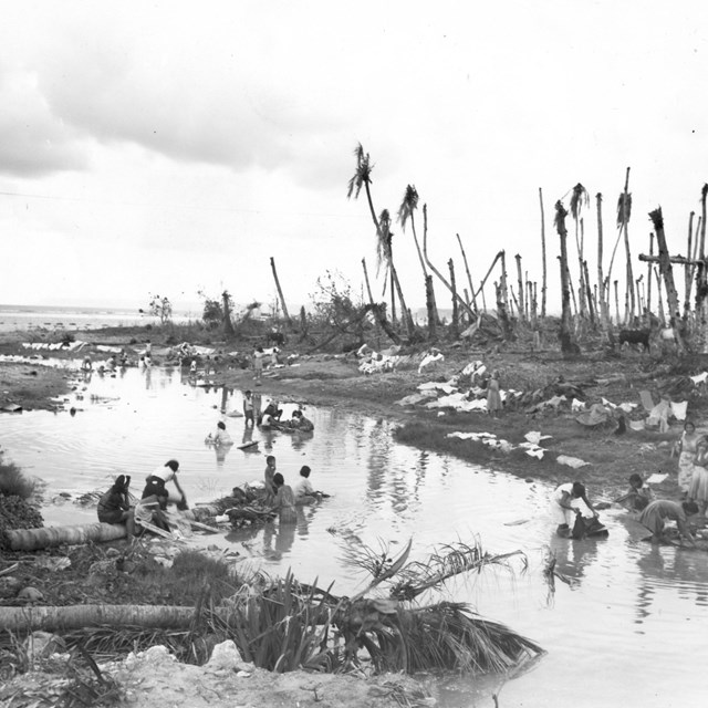 Women washing clothes in a creek next to bombed out palm trees