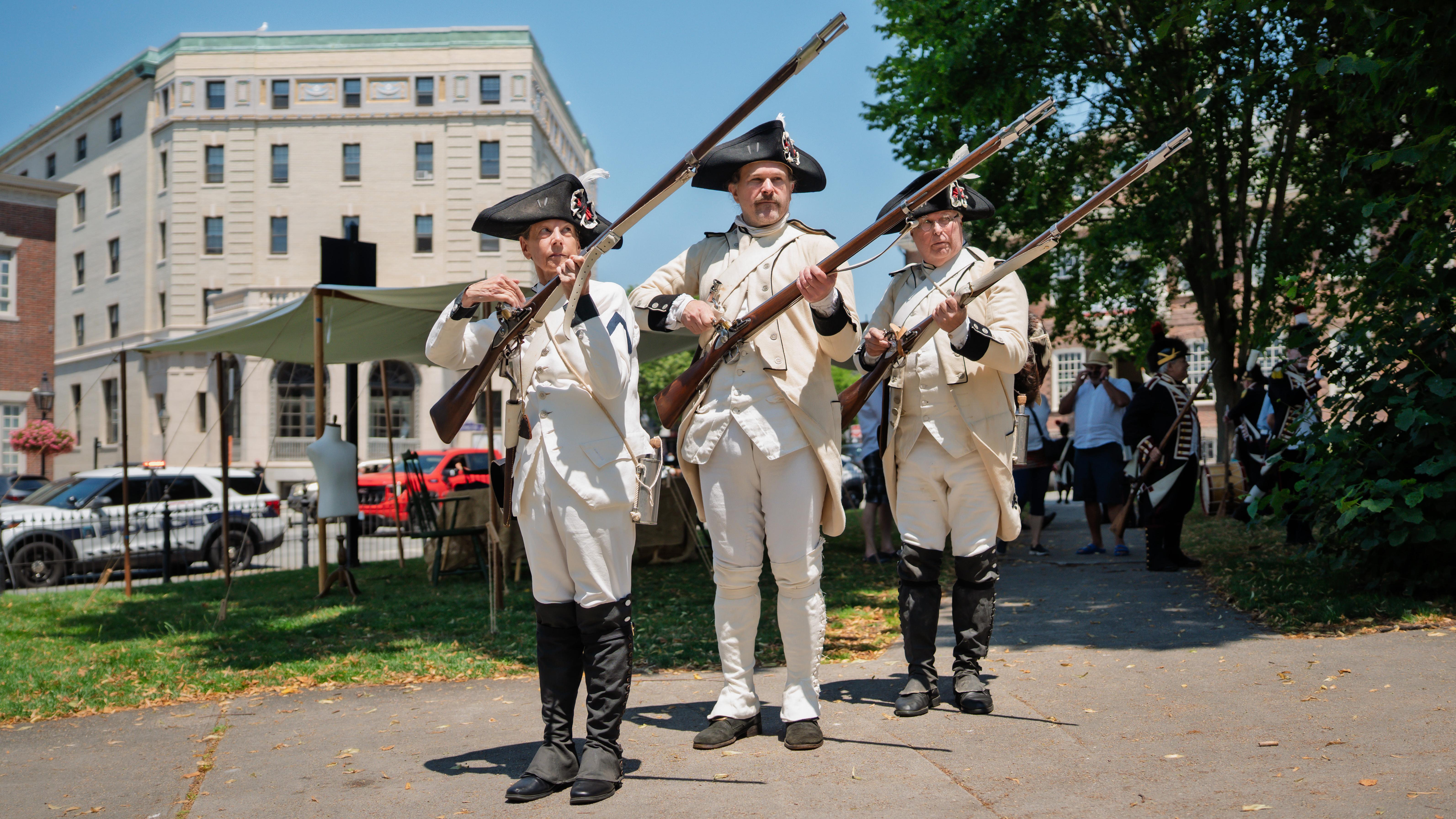 Three French military reenactors march with muskets during a living history event.