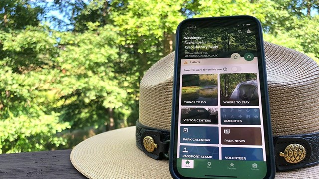 park ranger hat with NPS app open on cell phone trees in background