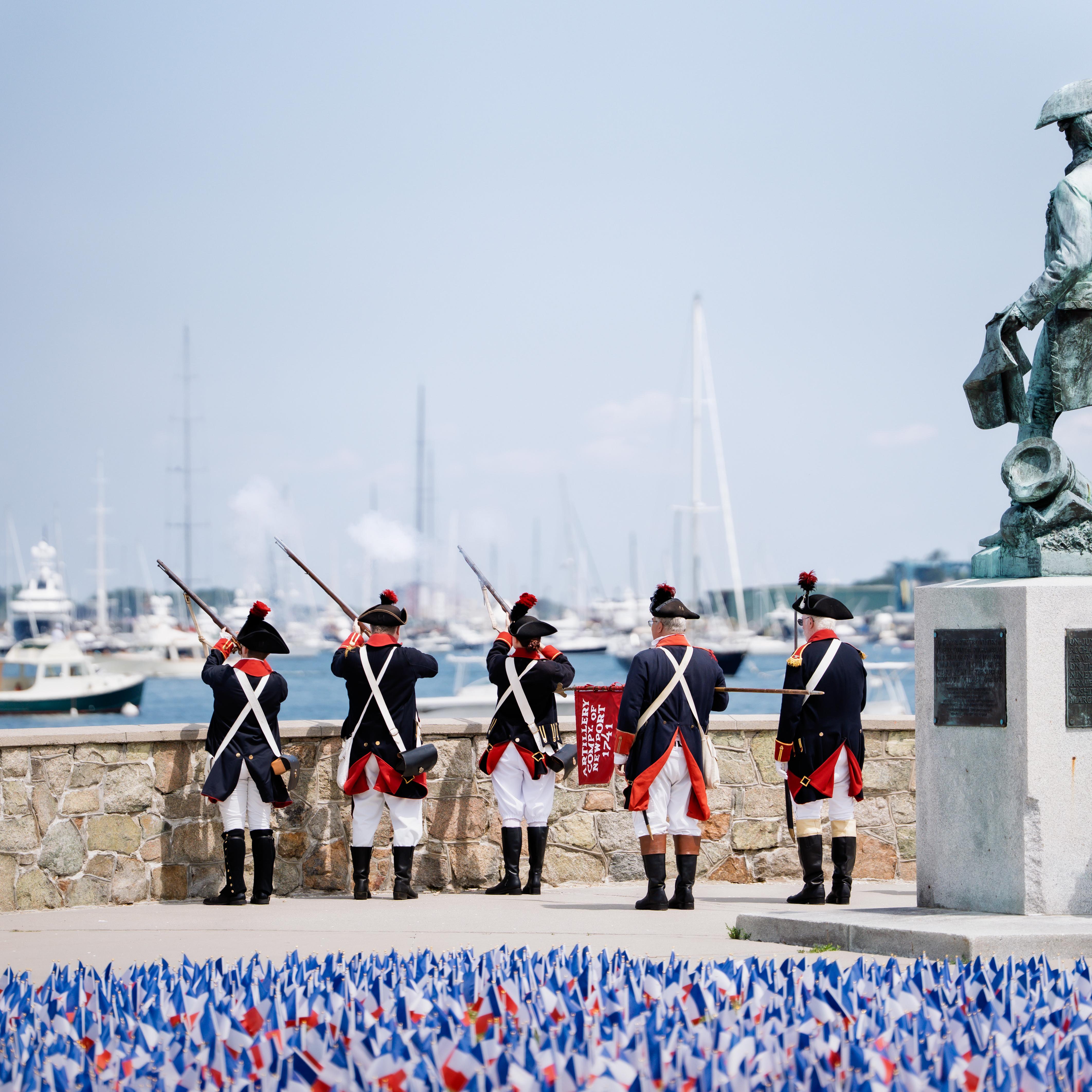 artillery company firing into bay with French flags in foreground and Rochambeau bronze statue