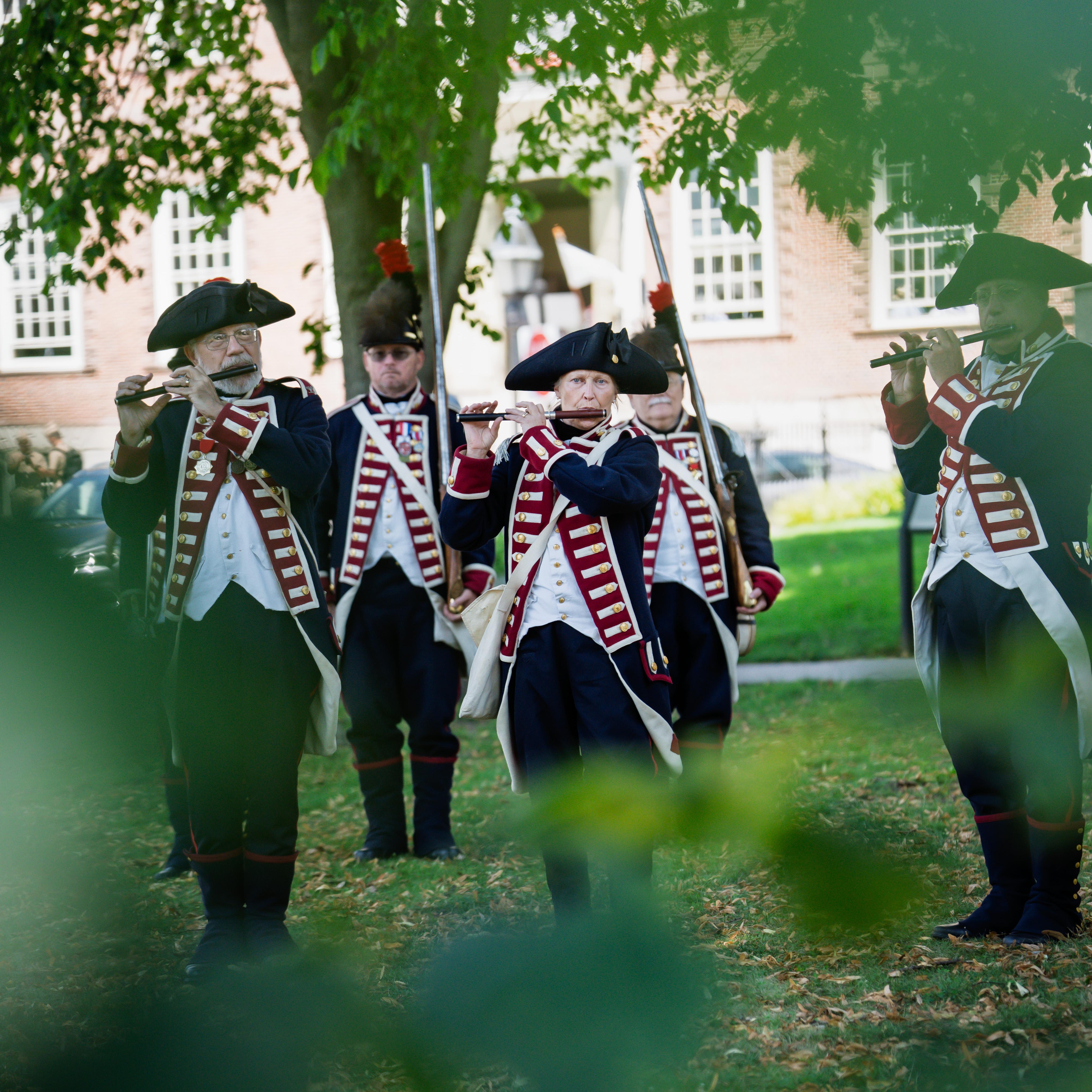 military band playing in square with green leaves in the front.