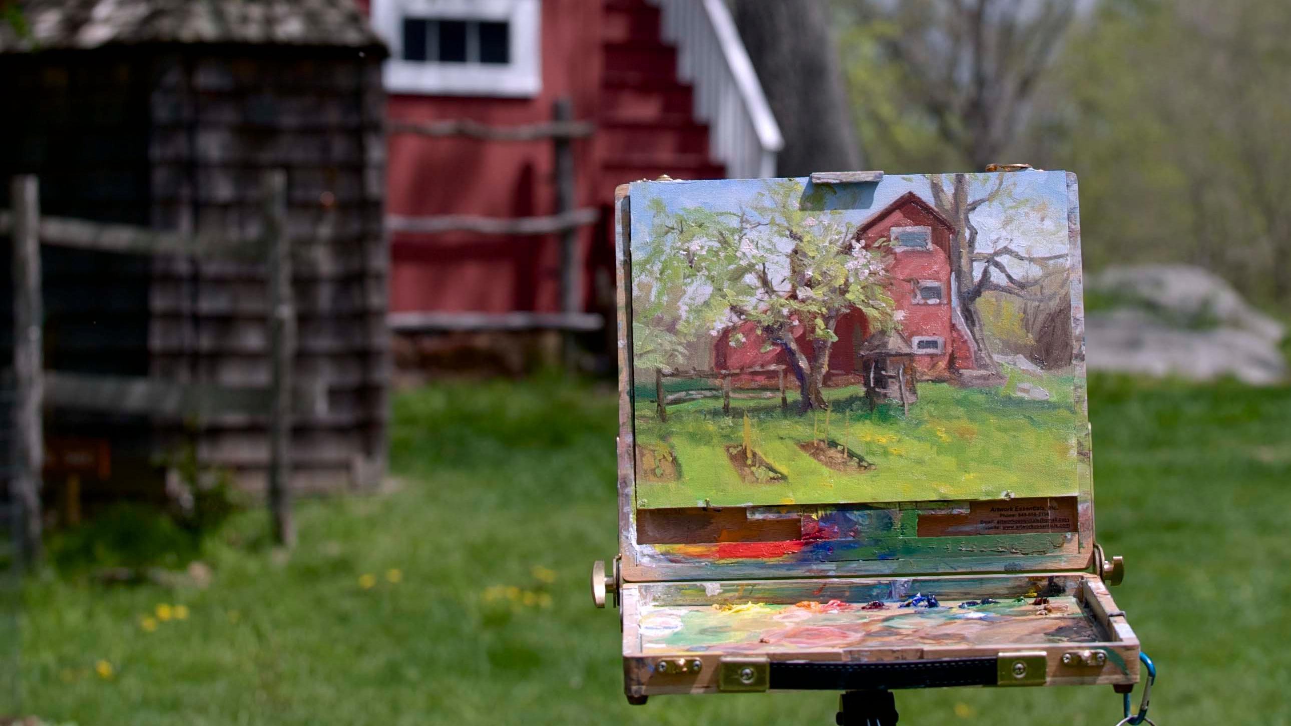 An easel with a painting of a historic building set up outside, with the building in the background