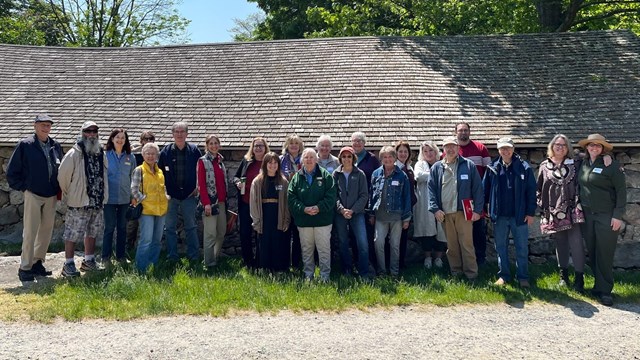 a group of artists stand in front of a woodshed for a picture.