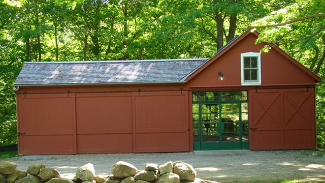 a small red building with glass doors in front of green woods.