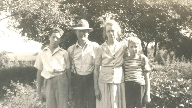 A family of four, mom, day and two young sons standing next to one another outside.