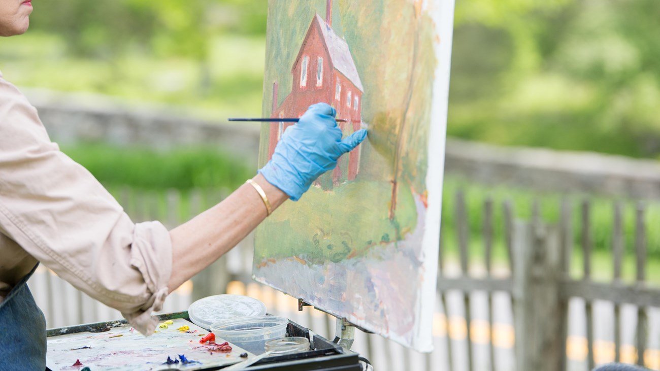 A painter creating art work based of a red building in front of them on a canvas