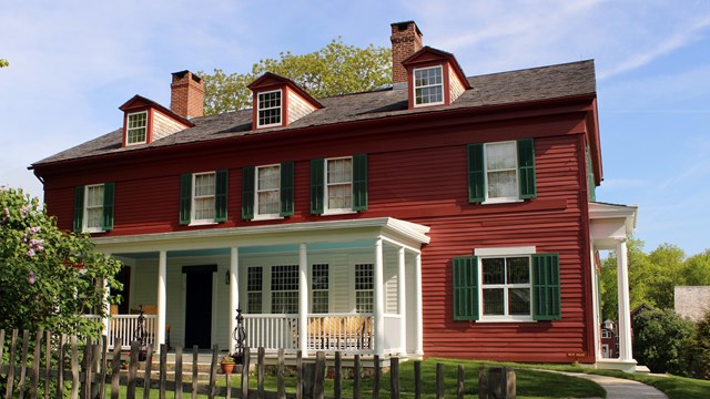 A large, red historic house with green shutters and a white porch. 
