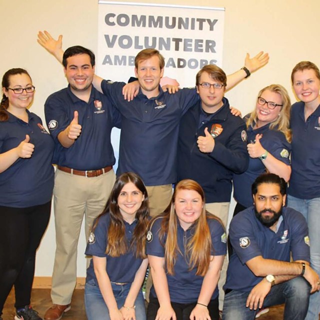A group of young people in matching blue shirts smile and give thumbs up.