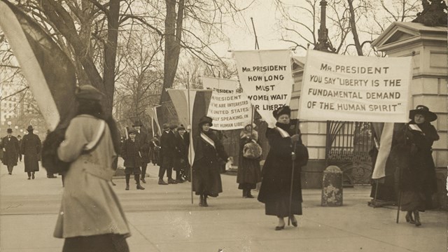 Women suffragists protest in a picket line outside the White House fence.