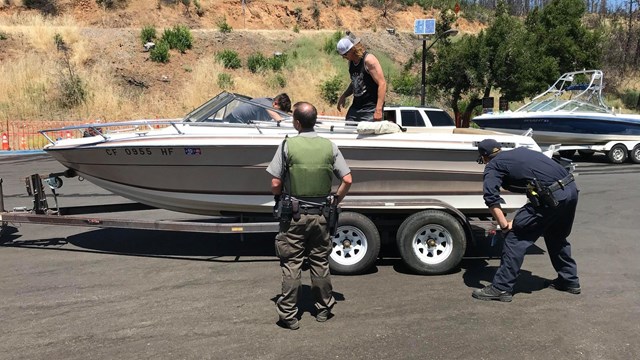 A law enforcement ranger in green and gray uniform inspecting a motorboat.