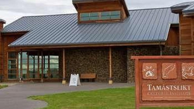 A stone and wood building with large windows. In front a sign reads "tamastslikt cultural institute"