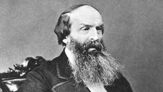 Black-white portrait: a man in a suit sitting in a chair. He is mostly bald with a large grey beard 