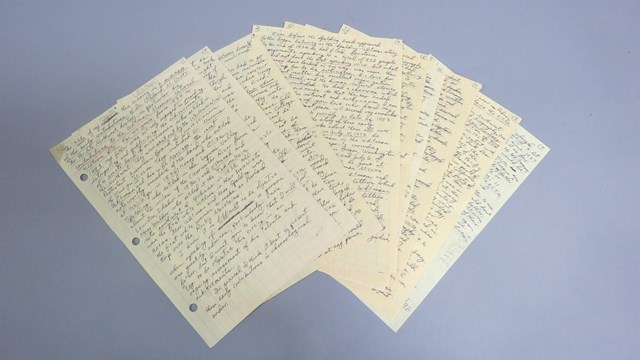 Several handwritten pages are laid flat in an arc shape on a grey flat surface.