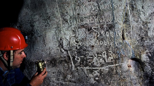A caver observes signatures left on a cave wall.