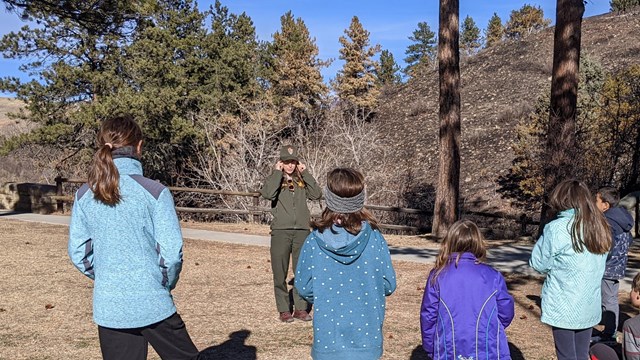 A ranger showing a group of kids an animal skull on the front lawn of the visitor center.