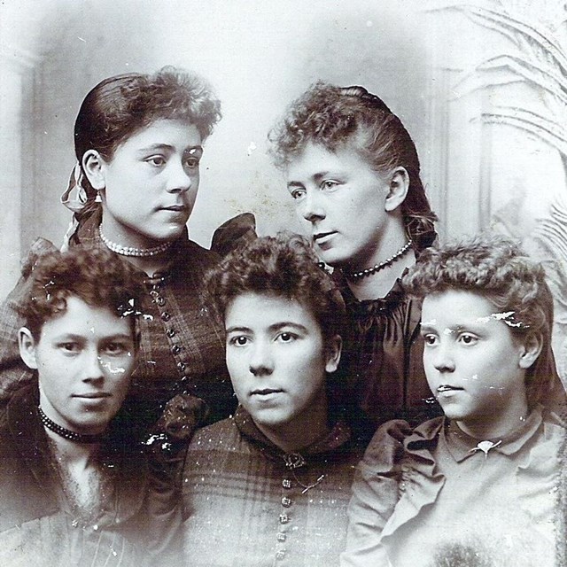 a black and white portrait of five young girls with curly braided hair wearing dresses