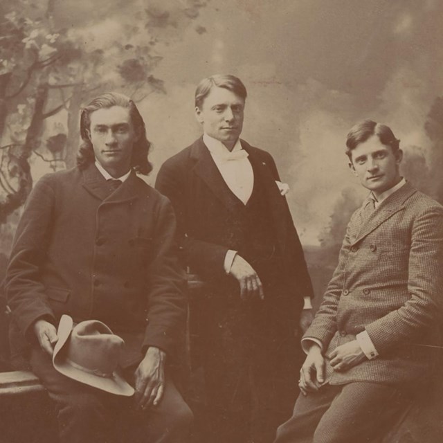 a sepia photo of three men in old-fashioned suits posing against a backdrop