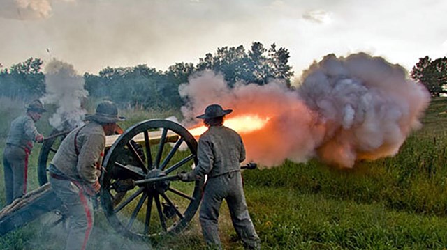 Living history actors fire artillery. Smoke and fire come out the end of the barrel. 