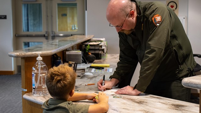 Boy stands in front of a ranger with his right hand raised for the junior ranger pledge. 