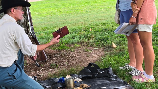 Ranger dressed in living history clothes gestures to group of children. 