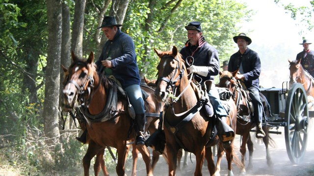 Men dressed in Civil War attire ride horses as they pull artillery behind them. 