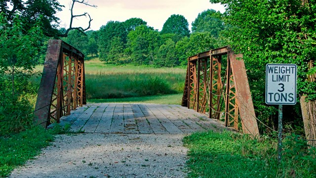Sign in front of an old steel bridge reads "weight limit 3 tons".