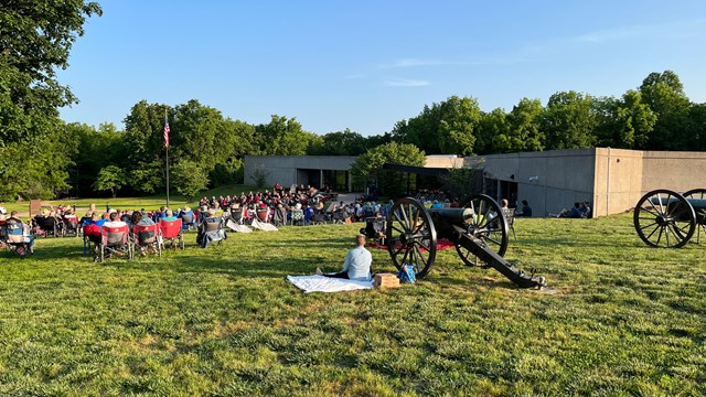 Cannons in the foreground a crowd and a band in front.