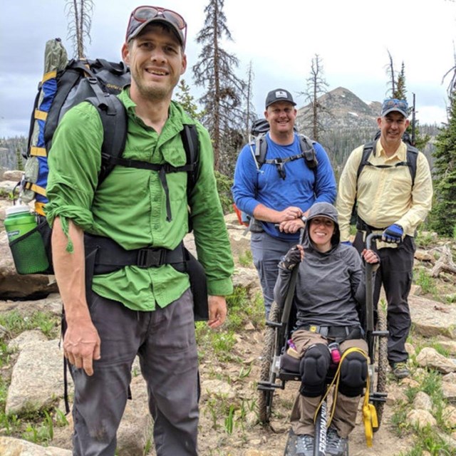 A group of hikers stand on a hilltop in trees.