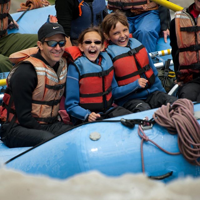 Family of kids and adults on a raft in river rapids.