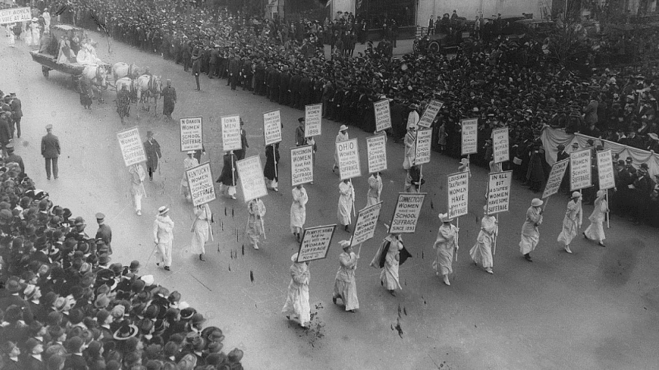 Aerial photo of women marching in parade with spectator-lined street. Library of Congress. 
