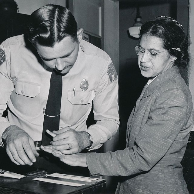 Male police officer fingerprinting a woman.