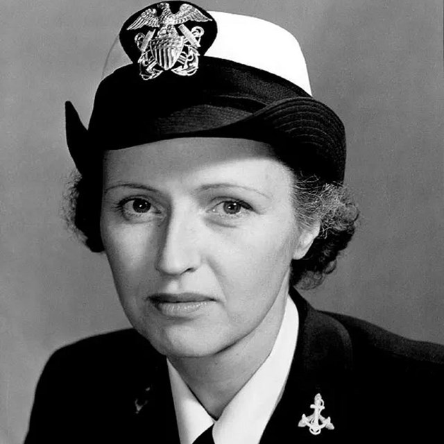 A white woman in a military cap and jacket faces the camera