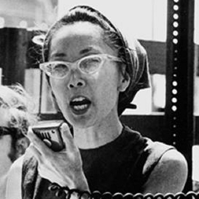 Asian American woman with cat eye classes holds megaphone speaker