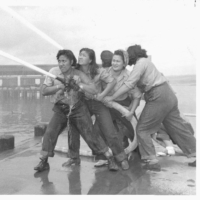 Five women holding a firehose and looking up into the distance