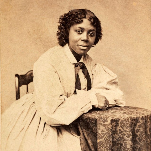 Black woman seated in light colored dress