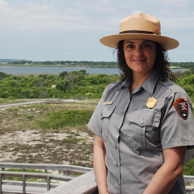 A park ranger in uniform stands in front of a landscape