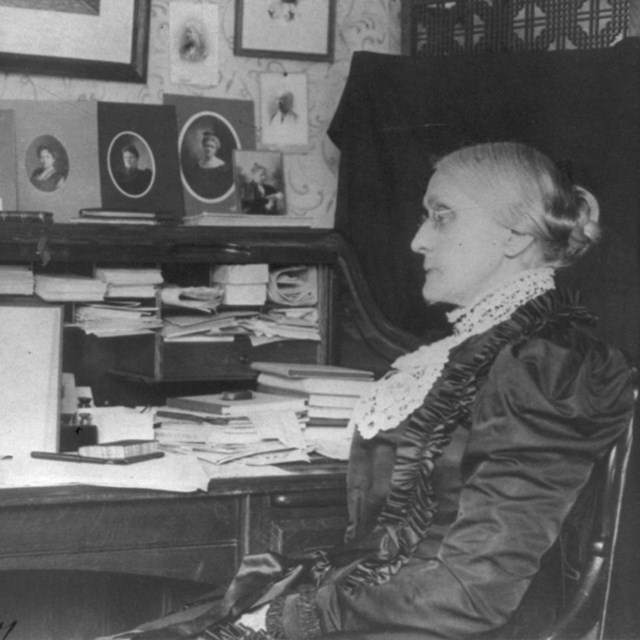 Susan B Anthony seated at a desk. Black and white photo