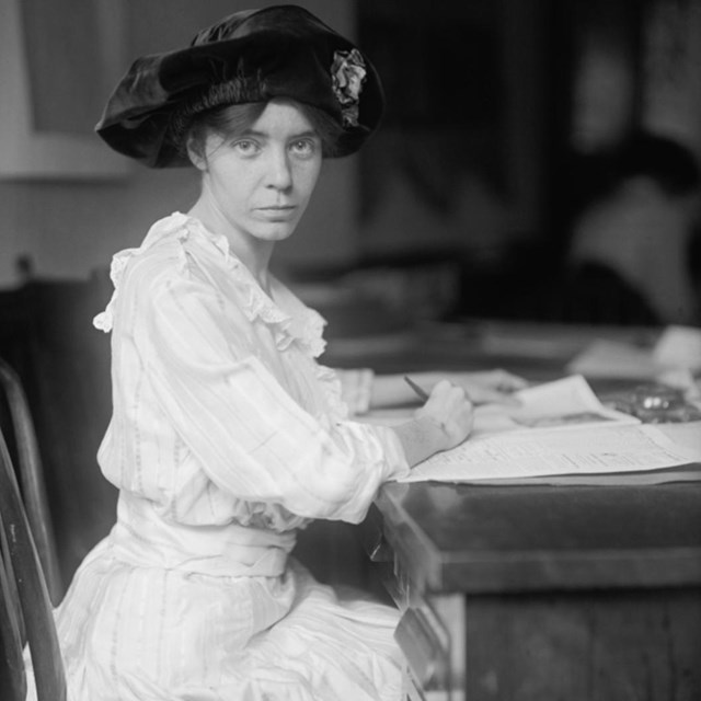 Black and white photo of Alice Paul sitting at a desk