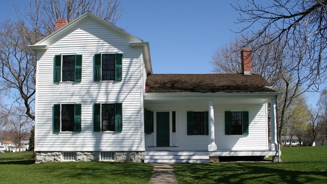 A two-story white house with a porch and green shutters.