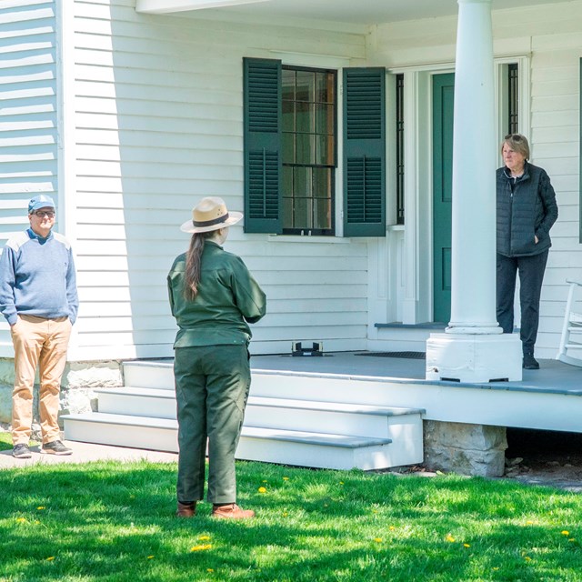 A ranger standing in front of a porch speaking to people.