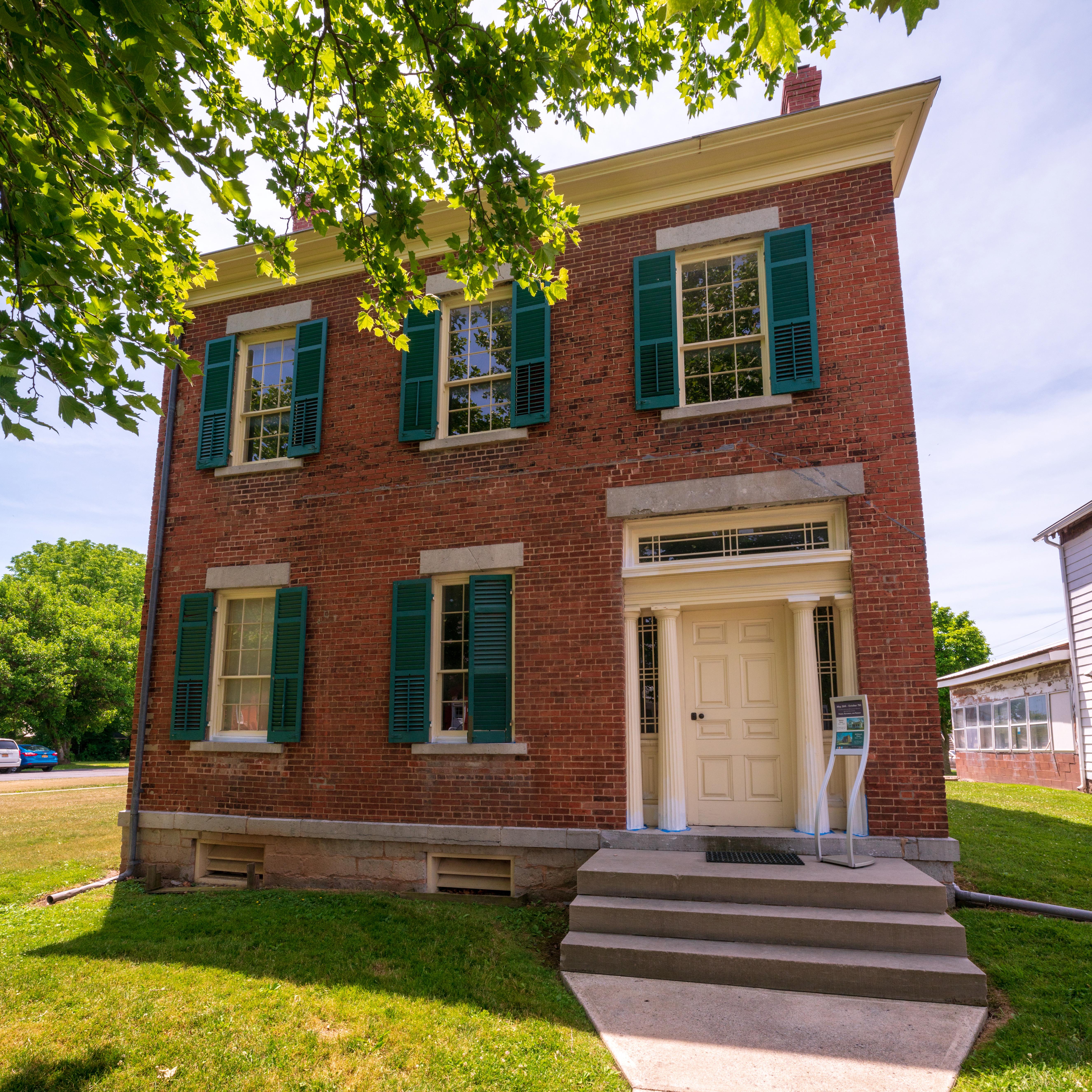 A two-story red brick house with green shutters.